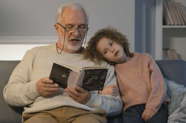 Grandad providing childcare to granddaughter and reading a book to her