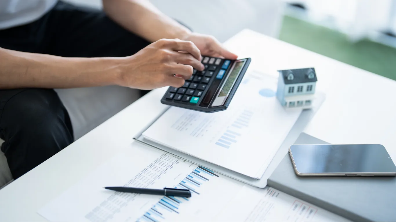 Inheritance tax and pensions blog - decorative image oh a person using a calculator with a model house and documents on table