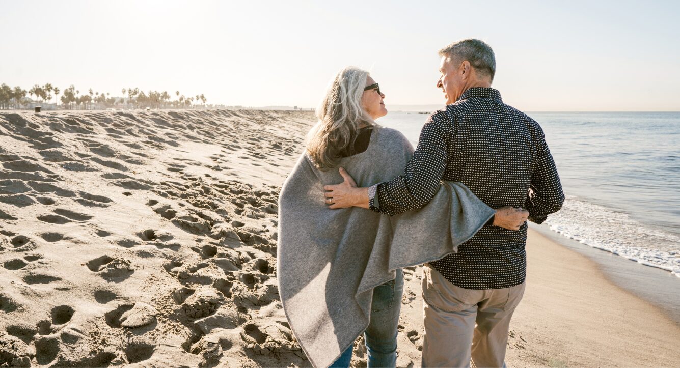 pension access age rising couple walking on the beach at sunset